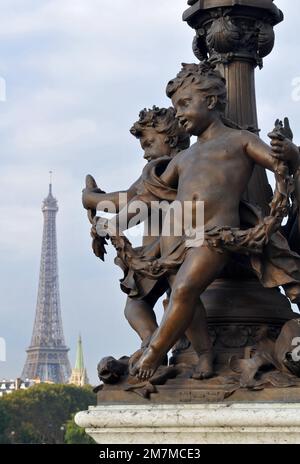 The Eiffel Tower stands in the background behind bronze sculptures at the base of a lamp on the Pont Alexandre III bridge in Paris. Stock Photo