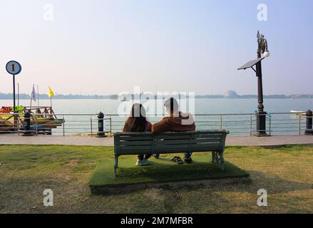 Rear View of a couple sitting on a bench facing lake. Sunny day. Stock Photo