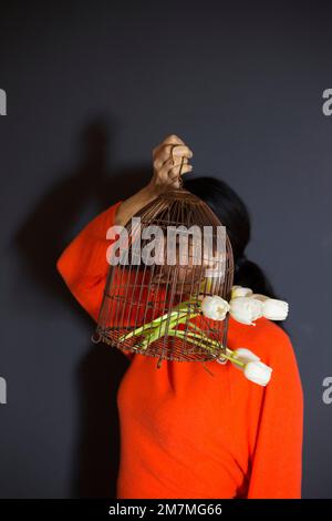 Dark haired woman with antique bird cage filled with white tulips Stock Photo