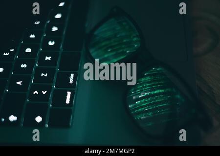 Portrait and close up of glasses on laptop with the light of screen with green binary numbers Stock Photo