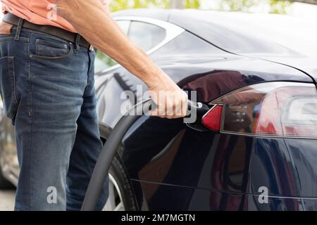 Man plugs in the charging cable to charge his Tesla Stock Photo