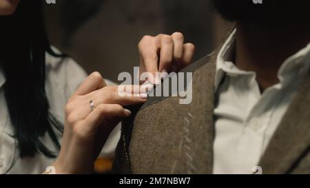 Female seamstress works on business or wedding suit. African merican businessman ordering tailored jacket in stylish luxury designer atelier. Concept of fashion and hand craft. Close-up shot. Stock Photo