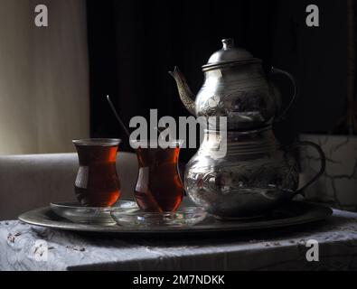 Traditional Turkish tea table in the loess room. Vintage copper tea pot and two glasses black tea on a tray. Stock Photo