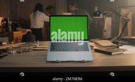 Cinematic shot of laptop with chromakey standing on table with tailoring tools in luxury designer atelier. Tailors discussing with African American client wedding suit on background. Fashion concept. Stock Photo