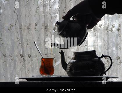 Traditional turkish tea with an old copper tea kettle on standing back light. A glass of tea light background. Stock Photo