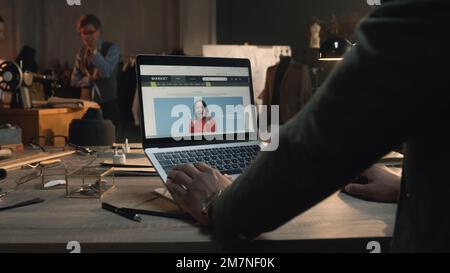 African American client in luxury designer atelier browsing online shop on laptop, watching clothing range, chooses sweatshirts. Concept of fashion and internet shopping. Close up view. Stock Photo