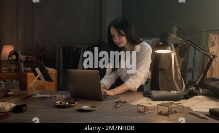 Female tailor works on new clothes collection in luxury atelier. She draws modern design of tailored suits on computer and tablet, chooses color and type of textile. Concept of fashion. Slow motion Stock Photo