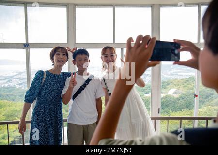 A boy using his mobile phone to take a picture of three people, a 13 year old boy, his mother and a friend. Stock Photo