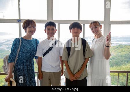 Four Japanese people, two boys and two mature women on a day out, posing for a photograph, side by side, on a viewing platform. Stock Photo