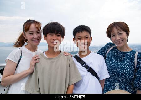 Four Japanese people on a outing, two mature women and two 13 year old boys, in a row, on a viewing platform. Stock Photo