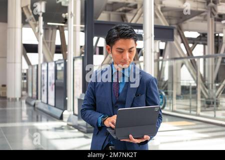 A young businessman in a blue suit on the move in a city downtown area, standing and using his digital tablet. Stock Photo