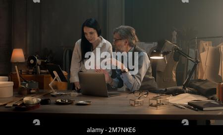 Tailors choosing design of tailored clothes collection on laptop and digital tablet computer. Colleagues working at modern workshop, talking about styles of garment, sewing type and color of cloth. Stock Photo