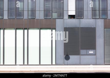 The arrangement of the blinds and wall elements of a building form a graphic pattern in white, brown and gray. Stock Photo
