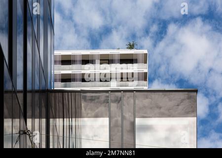 Sky and clouds are reflected in the glass facade of a high-rise building.  A  residential building  stands in the background. Stock Photo