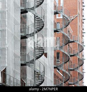 Several spiral staircases run along the outer wall of the building, and a scaffolding with safety net partially surrounds the brick building. Stock Photo