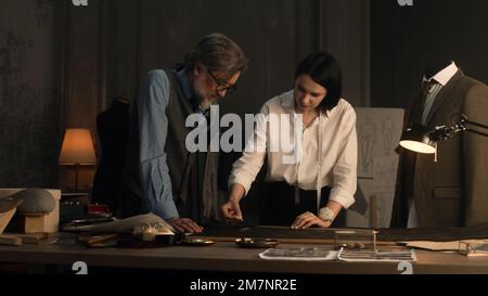 Male and female tailors working on sketch pattern of business or wedding suit. Mannequin with tailored shirt and jacket in stylish luxury designer atelier or tailoring dim studio. Fashion concept. Stock Photo