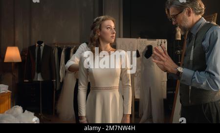 Cinematic shot of tailors taking measurements of woman for wedding dress. Bride on fitting wedding dress in luxury designer atelier or tailoring studio. Concept of fashion, handmade and couturier. Stock Photo