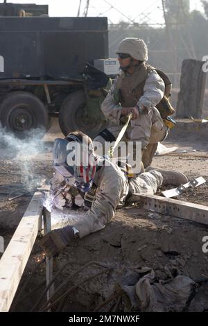 041116-M-1250B-008. [Complete] Scene Caption: US Navy (USN) Seabee PETTY Officer 1ST Class (PO1) Hector Calderon (right), Kalsu Detachment (Det), Naval Mobile Construction Battalion 4 (NMCB-4), 24th Marine Expeditionary Unit (MEU), holds a strap attached to the harness worn by USN Seabee PETTY Officer 2nd Class (PO2) Jim Muskevitsch, Kalsu Det., NMCB-4, 24th MEU, in order to secure PO2 Muskevitsch as he solders a support beam into a mortar impact crater as they work on a bridge that they are reconstructing in Mahmuydiyah (Babil Province), Iraq, which was severely damaged from repeated attacks Stock Photo