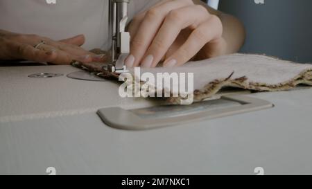 Hands of female seamstress works with fabric on sewing machine. Woman sews clothes in atelier workshop or at home. Concept of fashion, tailoring industry, handmade and self-employment. Close-up shot. Stock Photo