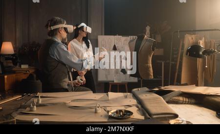Tailors wearing VR headset with wireless controllers. They working in luxury atelier or tailoring workshop and creating weeding suit in virtual reality. Concept of technologies of future in business. Stock Photo