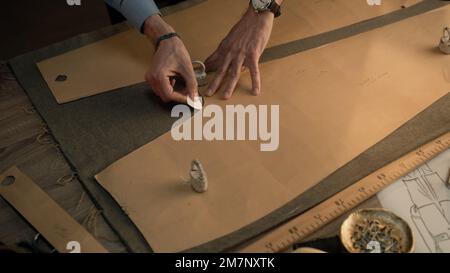 Male tailor draws sketch on fabric using paper stencil and soap for ...