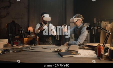 Multi ethnic tailors wearing VR headset with wireless controllers. They working in luxury atelier or tailoring studio and creating business suit in virtual reality. Concept of technologies in business Stock Photo