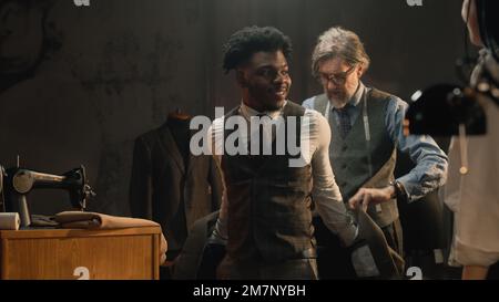 African American man on suit fitting in stylish luxury designer atelier or tailoring studio. Tailor puts jacket on man. Tailored wedding or business suit. Concept of fashion, handmade and couturier. Stock Photo