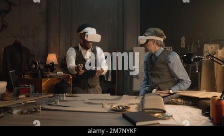 Multi ethnic tailors wearing VR headset with wireless controllers. They working in luxury atelier or tailoring studio and creating business suit in virtual reality. Concept of technologies in business Stock Photo