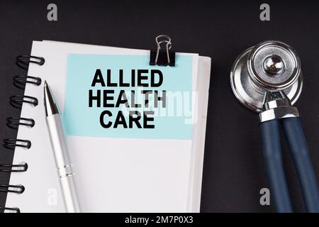 Medical concept. On a black surface, a stethoscope, a notebook, a pen and a blue sticker with the inscription - Allied Health Care Stock Photo