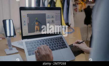 Female fashion designer develops future design of clothes in 3D modeling program on laptop using digital tablet and stylus. She works in atelier workshop. Fashion and technologies in business concept. Stock Photo