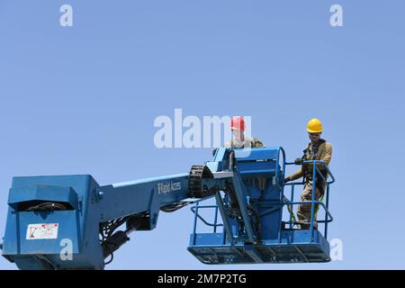 (From left) Airman 1st Class Christian Hudson and Staff Sgt. Philip Atutor, structural specialists with the 380th Expeditionary Civil Engineer Squadron structures shop, operate a boom lift May 11, 2022 at Al Dhafra Air Base, United Arab Emirates. They were performing maintenance on a pavilion’s sunshades which were damaged in a windstorm. Stock Photo