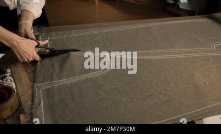 Professional female tailor cuts fabric according to sketch using scissors for sewing. Process of making clothes in luxury designer atelier or tailoring studio. Fashion and hand craft concept. Stock Photo