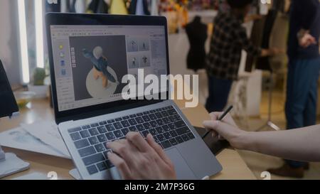 Female fashion designer develops future design of clothes in 3D modeling program on laptop using digital tablet and stylus. She works in atelier workshop. Fashion and technologies in business concept. Stock Photo