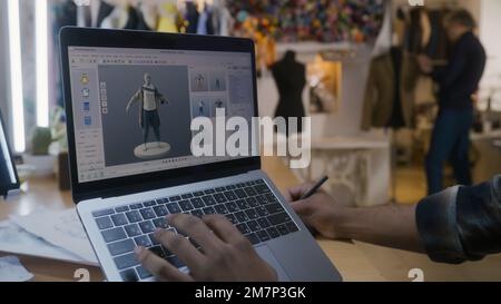 African American fashion designer creates clothes in 3D modeling software on laptop using digital tablet and stylus. He works in atelier workshop. Concept of fashion and technologies in business. Stock Photo