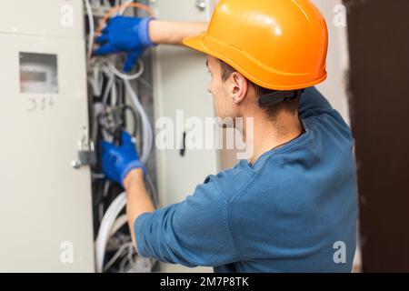 Close up shot of hand of aged electrician repairman in uniform working, fixing, installing ethernet cable in fuse box, holding flashlight and cable Stock Photo