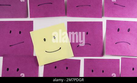 Uhhappy faces with one happy face on paper office sticky note in purple and yellow color Stock Photo