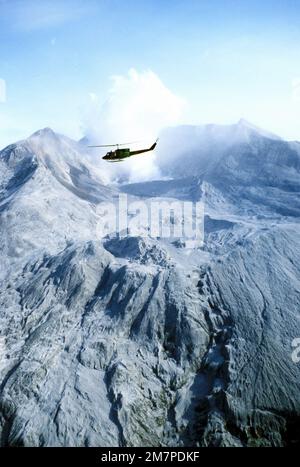 Left side view of a UH-IN Iroquois helicopter from the 304th Aerospace Rescue and Recovery Squadron in flight near the steam rising from the crater several days after a large eruption. Base: Mount Saint Helens State: Washington (WA) Country: United States Of America (USA) Stock Photo