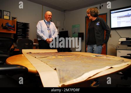 Susan Anderson (right) provides some insights to the State of Indiana flag that she is donating as an artifact to the Hampton Roads Naval Museum to Museum Educator Zach Smyers (left). The flag belonged Anderson’s father, the late Captain Walter “Jack” Deal, USN, who was the Commanding Officer of River Assault Squadron 15 during the Vietnam War. At the time, it was customary for boat captains to fly the state flag of their home state on their river assault boats during the Vietnam War. Stock Photo