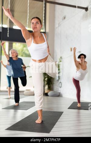 European woman and group of sporty people practicing yoga lesson at sport studio Stock Photo