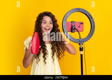 Child vlogger making video blog on phone. Teen girl blogger influencer recording video for social media, hold hair conditioner or shampoo bottle Stock Photo