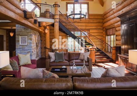 Brown leather and burgundy sofas, wooden coffee table in living room with medieval style chandelier inside luxurious Scandinavian log home. Stock Photo