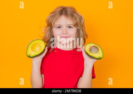 Kids face with fruits. Kid hold red avocado in studio. Studio portrait of cute child with avocado isolated on yellow background. Stock Photo