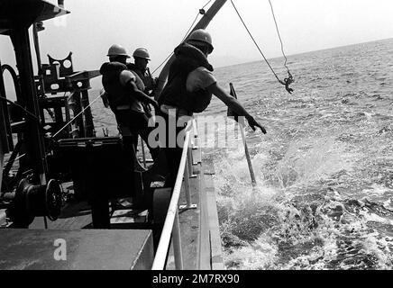 Three crewmen aboard minesweeping boat 51 (MSB-51) prepare to drop a ...