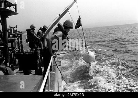 Three crewmen aboard minesweeping boat 51 (MSB-51) look toward the ...