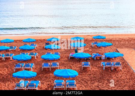 Beach umbrellas in a row . Blue beach umbrellas and chaise longue . Sandy coast and calm water Stock Photo