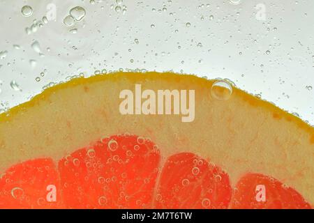 Close-up of a grapefruit slice in liquid with bubbles. Slice of red ripe grapefruit in water. Close-up of fresh grapefruit slice of red o on white bac Stock Photo