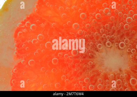 Close-up of a grapefruit slice in liquid with bubbles. Slice of red ripe grapefruit in water. Close-up of fresh grapefruit slice covered by bubbles. Stock Photo