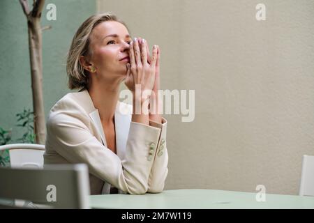 Worried woman thinking about something while sitting at a table outdoors. Stock Photo