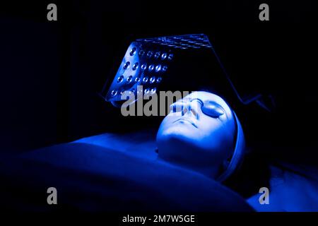 Young woman having blue LED light facial therapy treatment in beauty salon. Beauty and wellness concept. Stock Photo