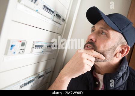 man pondering the fuses in a circuit breaker cabinet Stock Photo